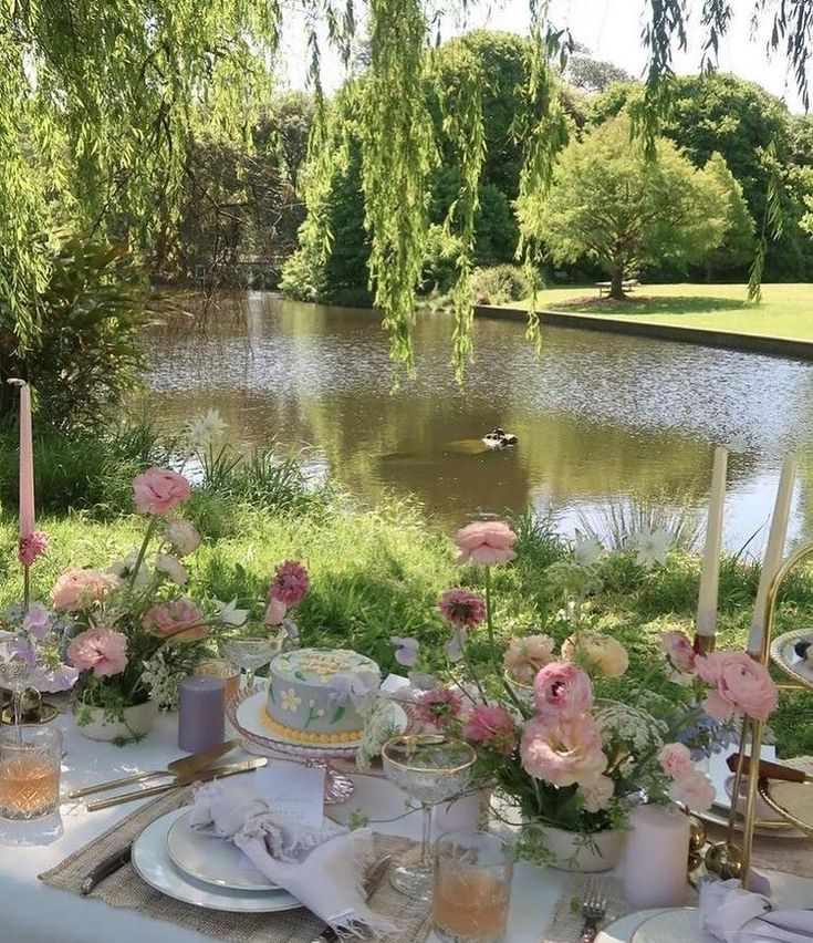 a table set up with flowers and candles for an outdoor dinner by the lake in summer