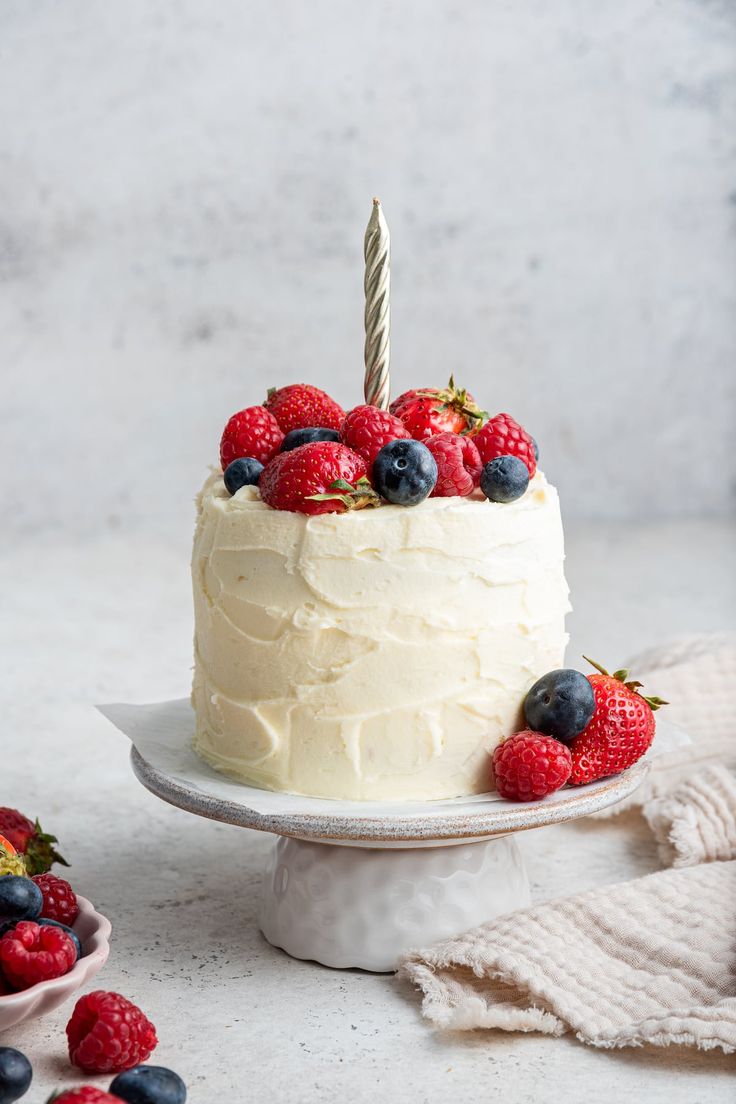 a white cake with berries on top and a single candle sticking out of the frosting