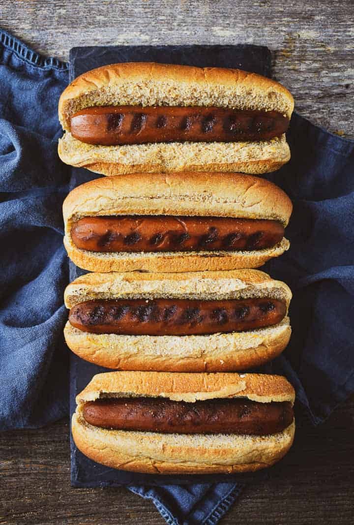 four hotdogs on buns sitting next to each other in front of a blue napkin