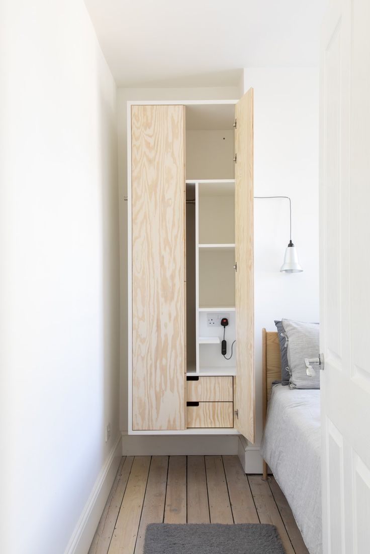 a bedroom with white walls and wood flooring has a built - in cabinet that opens up to the bed