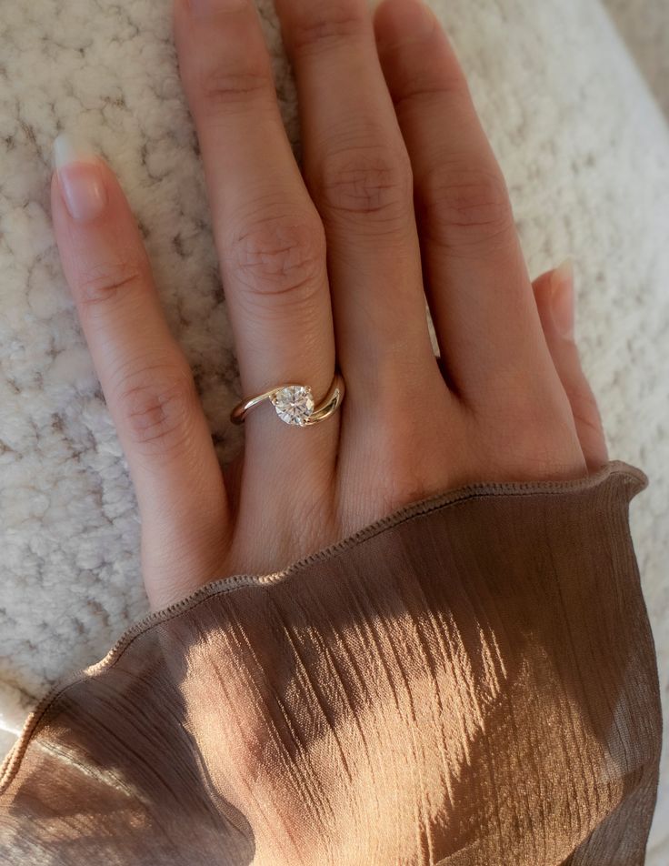 a woman's hand with a diamond ring on top of her left hand, resting against a white blanket