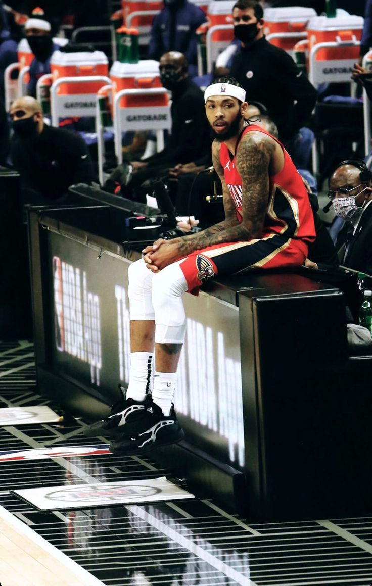 a man sitting on top of a bench in front of a basketball court with other people watching