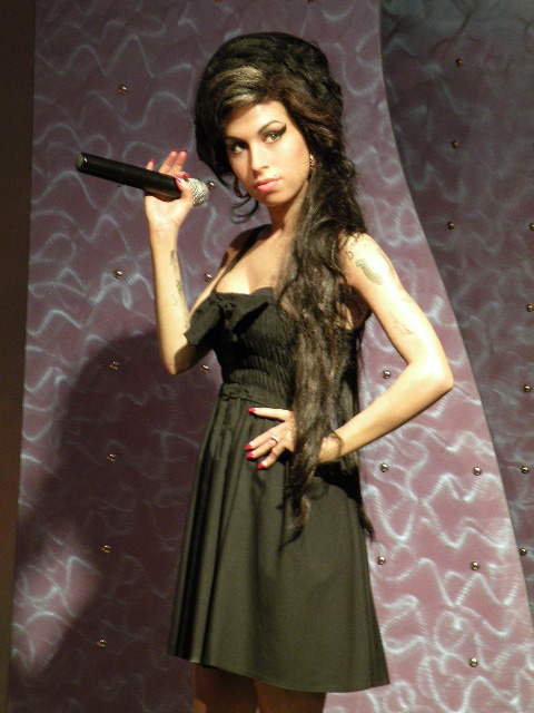 a woman with long hair holding a microphone in front of a purple wall and posing for the camera