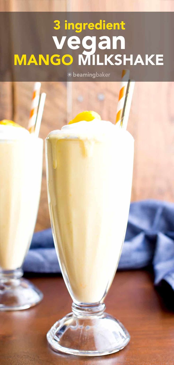 two glasses filled with mango milkshake on top of a wooden table