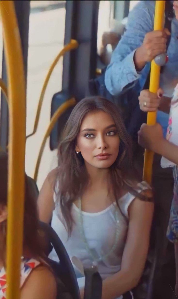 a woman sitting on a bus with other people behind her and holding onto the handle bars