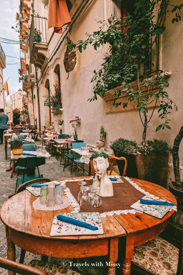 an outdoor restaurant with tables and chairs on the side walk, next to potted plants