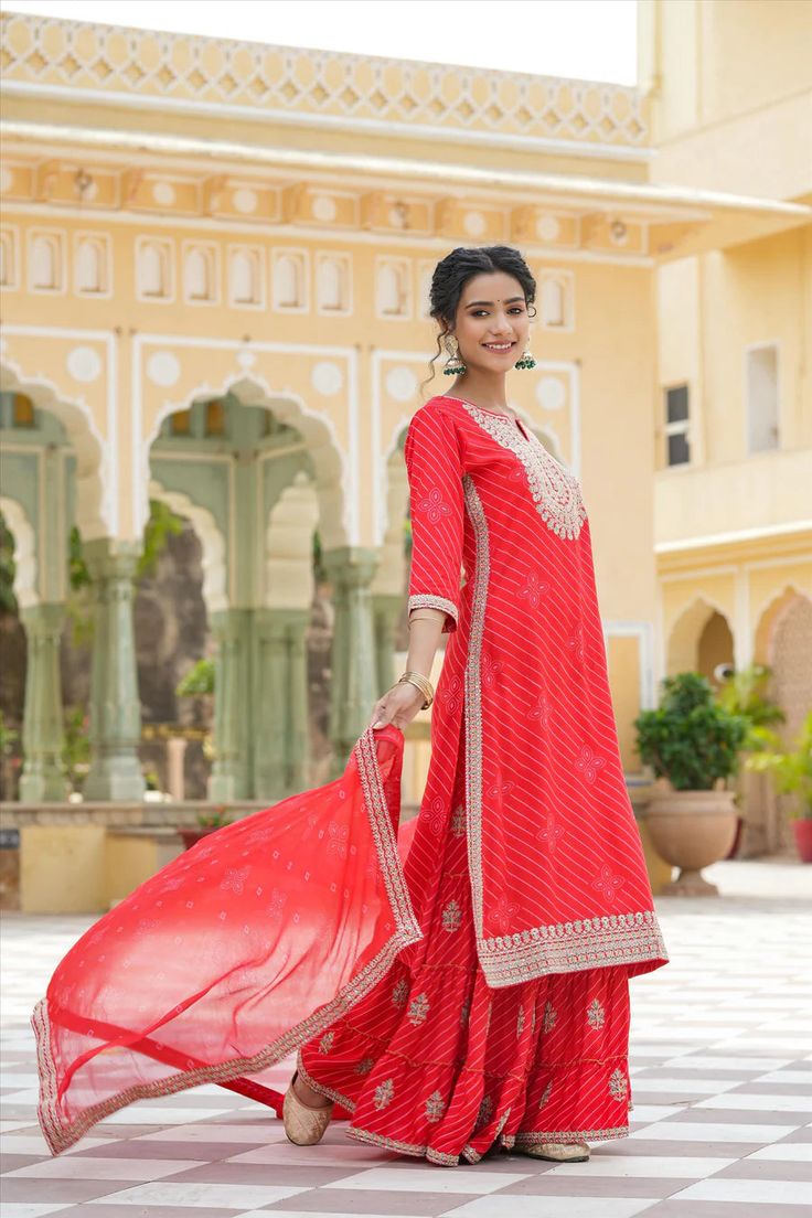 This Red Rayon Leheriya Embroidered Sharara Suit features a long kurta with Zari and Sequins embroidery accents on the yoke, sleeves, and hemline. The suit includes a coordinating sharara and a printed chiffon dupatta with an embroidered border for a unique, elegant look. Perfect for special occasions. Color: Red Top: Rayon Bottom: Rayon Dupatta: Chiffon Top Length: 46" Bottom Length: 41" Dupatta Size: 2.2 m Occasion: Festive Print-Pattern: Leheriya Ornamentation: Zari Shape: Straight Design Sid Phulkari Pants, Heavy Suits, Lucknowi Kurta, Gharara Suits, Patiala Salwar Suits, Embroidered Sharara, Bridal Dupatta, Phulkari Dupatta, Chikankari Suits