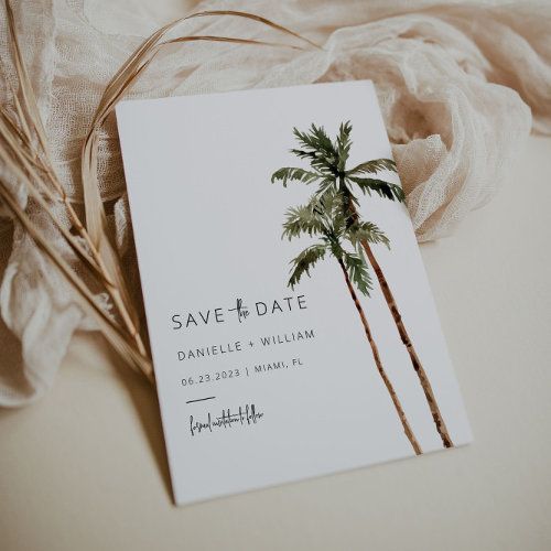 a save the date card with palm trees on it next to a white cloth and some feathers