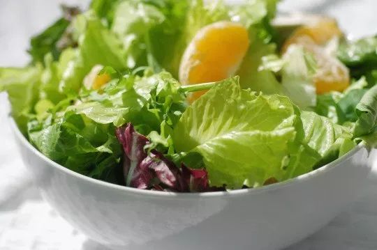 a white bowl filled with lettuce and oranges on top of a table