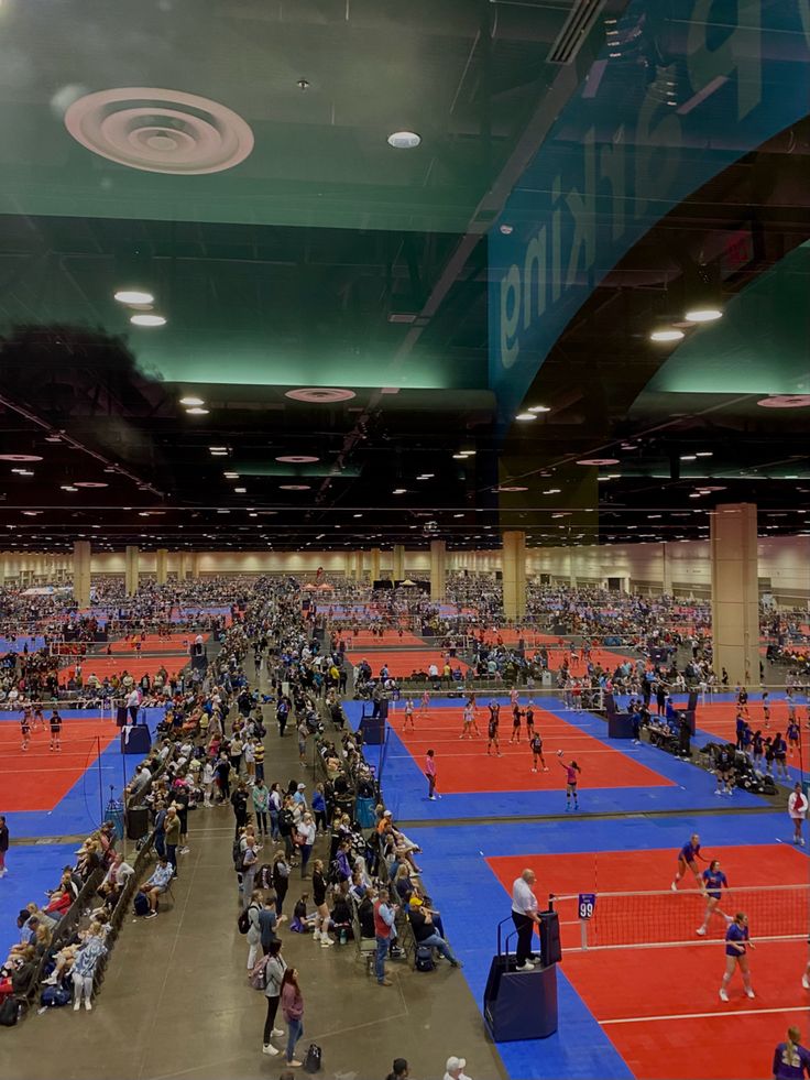 an indoor tennis court filled with lots of people on blue and red mats, surrounded by green ceilinging