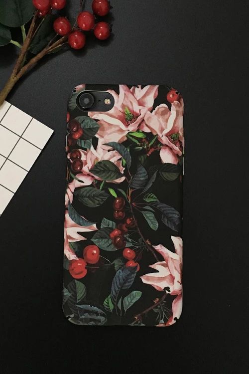 an iphone case with flowers on it next to a plant and some red cherries