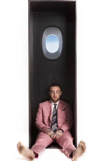 a man in a pink suit and tie sitting in a black box with his feet on the ground