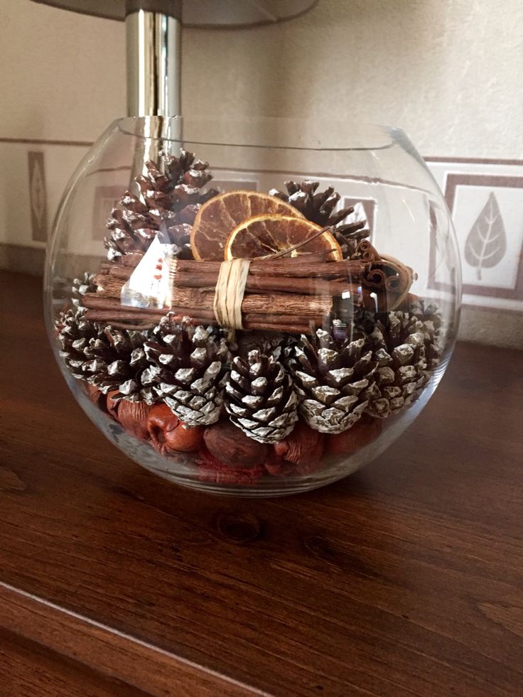 a glass bowl filled with pine cones, cinnamons and orange slices on top of a wooden table