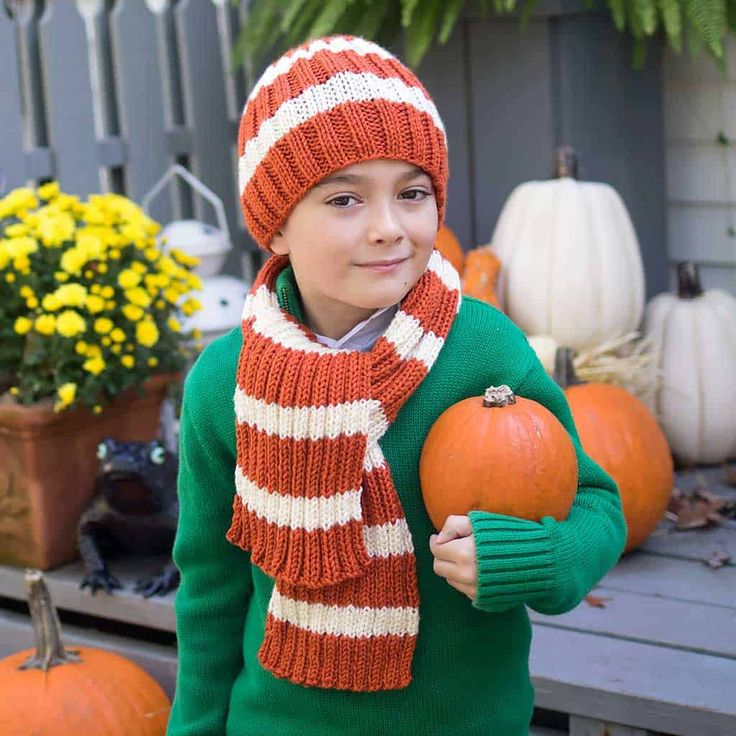 a young boy wearing a red and white striped scarf holding two pumpkins in his hands