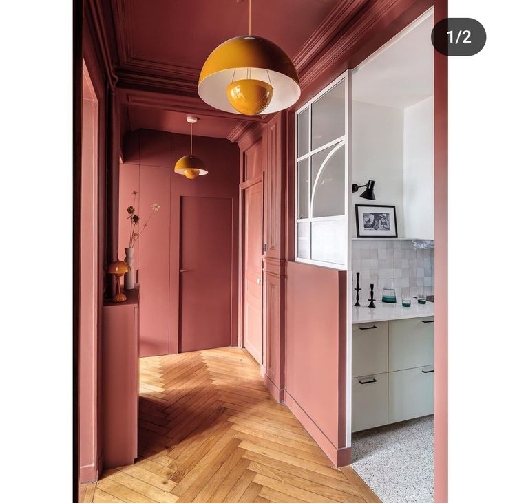 an empty hallway with pink walls and wood flooring is pictured in this image, there are two lamps hanging from the ceiling