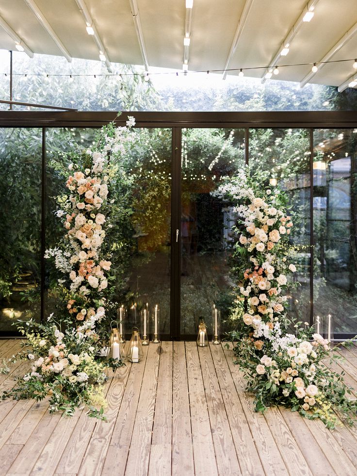 an outdoor ceremony with flowers and candles on the floor in front of glass doors that are open