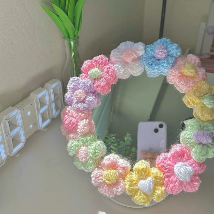 there is a cell phone in front of a crocheted wreath on the mirror