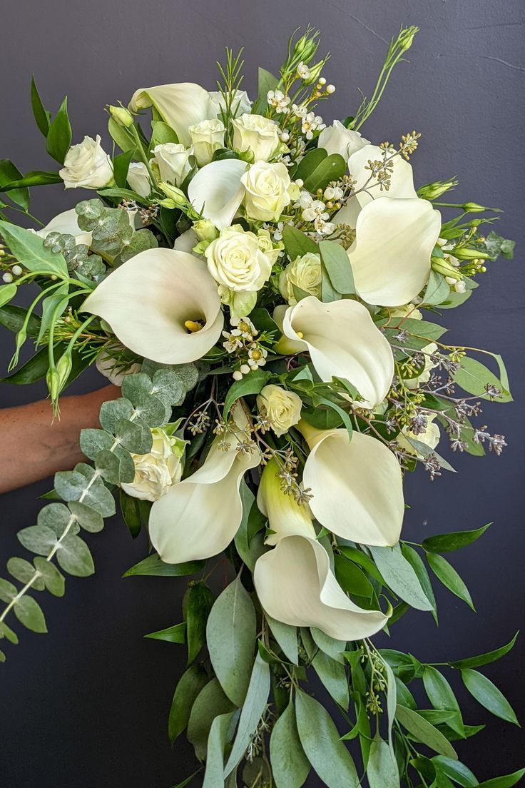 a bouquet of white flowers and greenery is being held by someone's hand