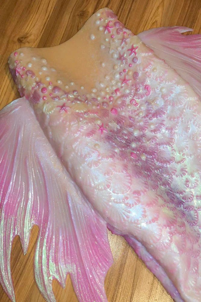 a pink and white fish with pearls on it's tail sitting on a wooden floor