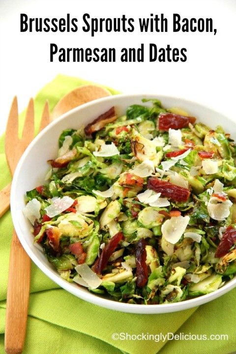 a white bowl filled with shaved brussels sprouts and dried cranberries next to wooden utensils