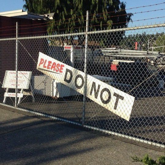 a sign that says please don't behind a chain link fence in front of a parking lot