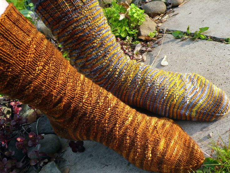 two knitted socks sitting next to each other on the ground in front of plants