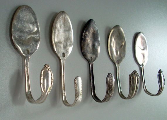 five spoons are lined up in a row on a white surface with hooks attached to them