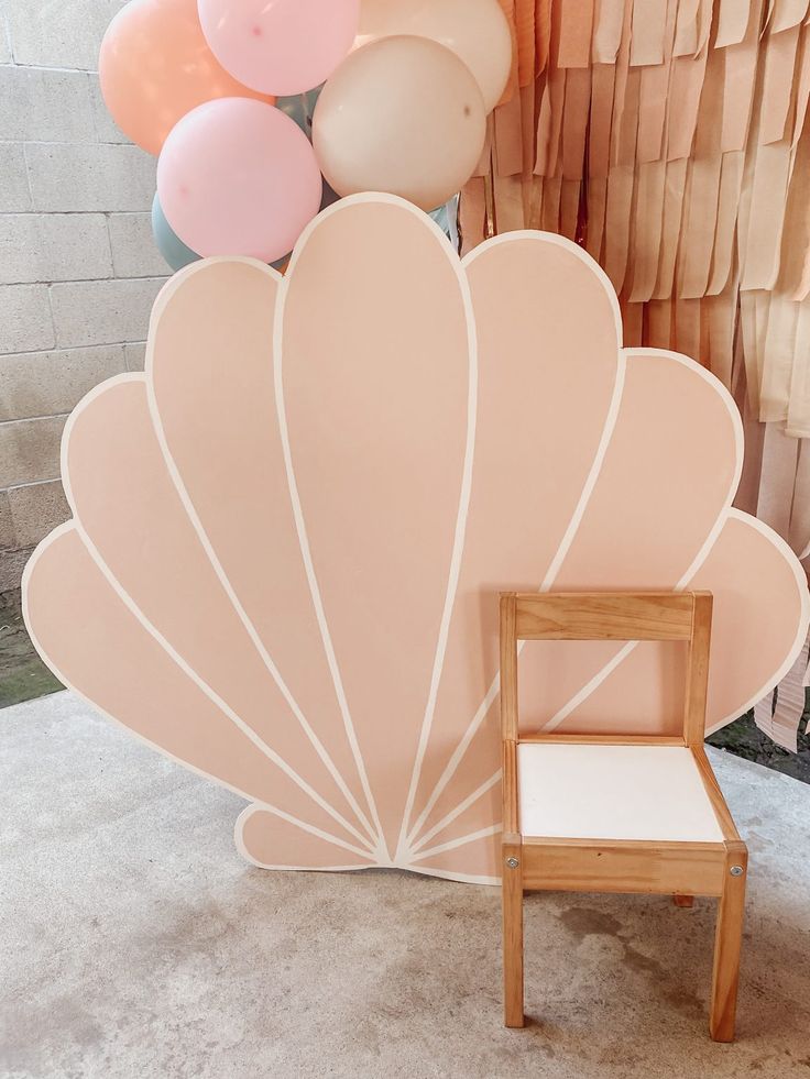 a chair sitting in front of a large shell shaped balloon wall with balloons behind it