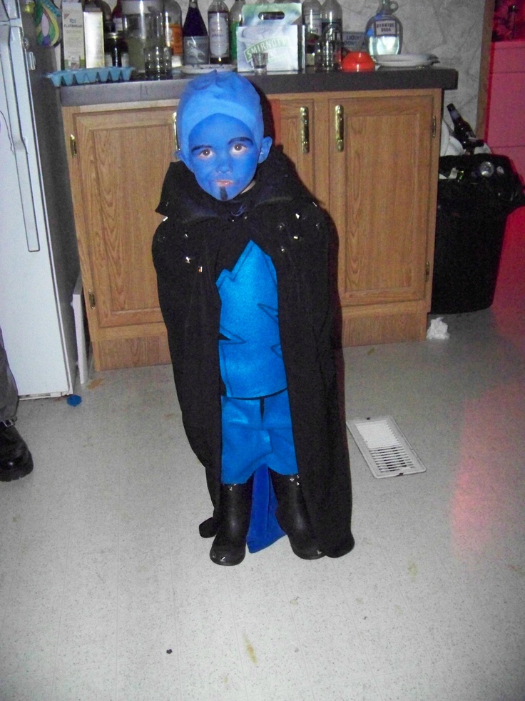 a young boy dressed in blue and black is standing in the kitchen with his hands on his hips