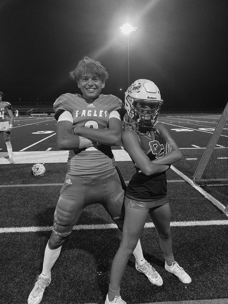 two female football players posing for a photo on the field at night with their arms around each other