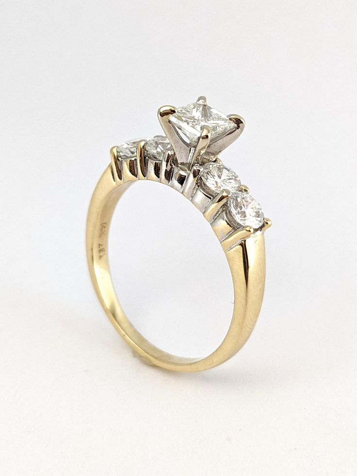 a three stone diamond ring on a white surface with the center setting in yellow gold