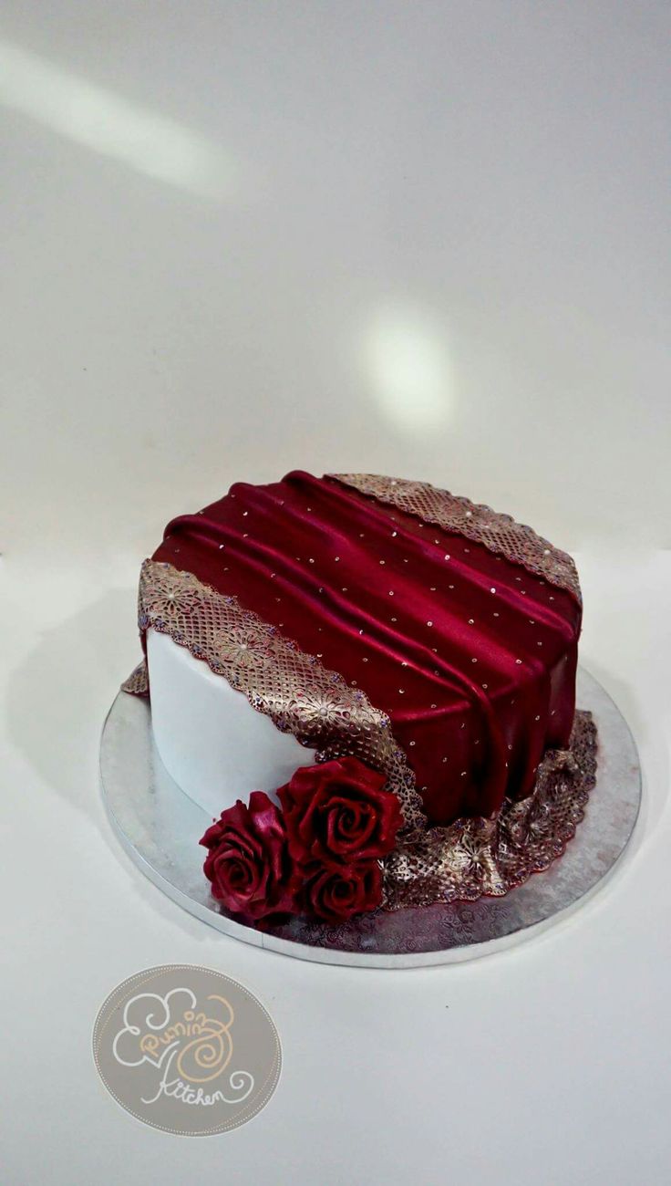 a cake with red frosting and flowers on it sitting on a white tablecloth