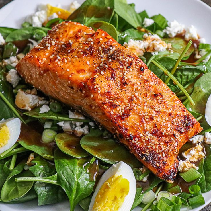 a white plate topped with salmon and salad next to hard boiled egg shells on top of spinach