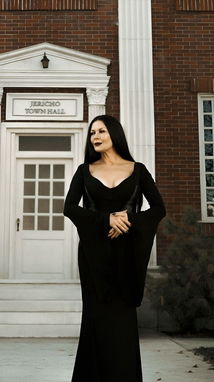 a woman standing in front of a building wearing a long black dress and holding her hands on her hips