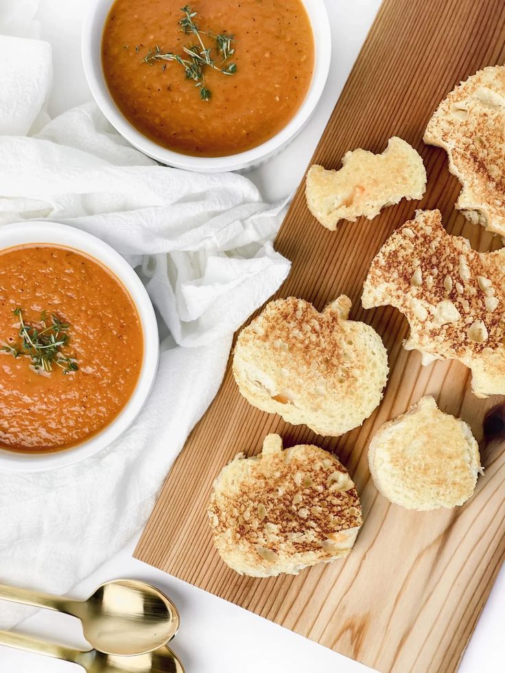 two bowls of soup and some bread on a cutting board