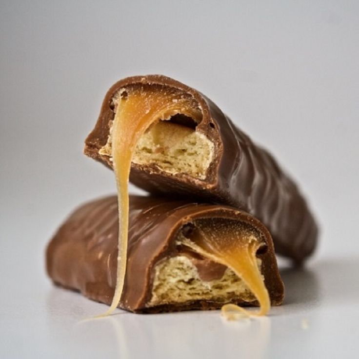 two pieces of chocolate covered in caramel on a white surface with a bite taken out