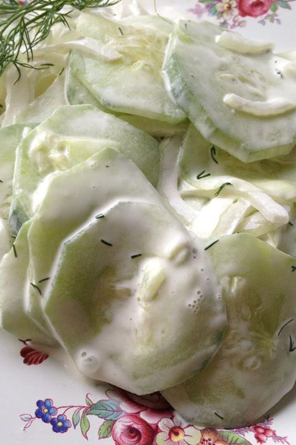 a white plate topped with cucumbers covered in sauce and dill sprigs