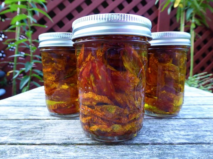 three jars filled with red and yellow liquid sitting on top of a wooden table next to plants