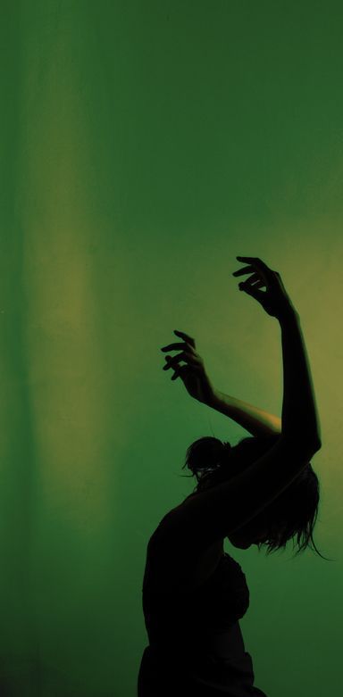 a woman standing in front of a green wall with her hands up to the side