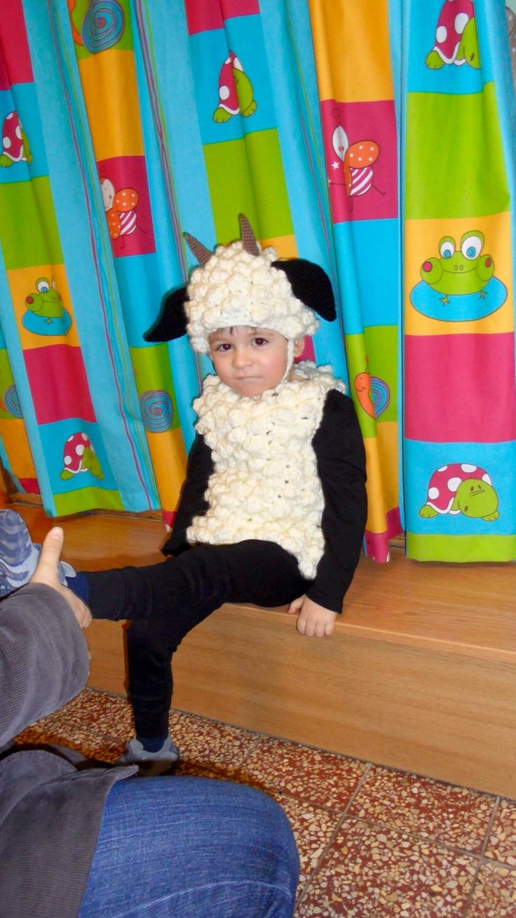 a young child wearing a sheep costume sitting on the steps in front of colorful curtains