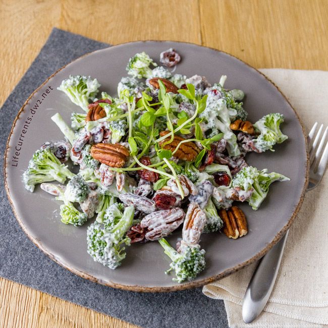 a white plate topped with broccoli salad and pecans on top of a wooden table