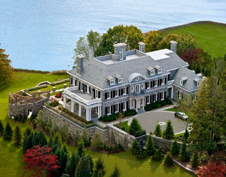 an aerial view of a large white house with trees and water in the back ground