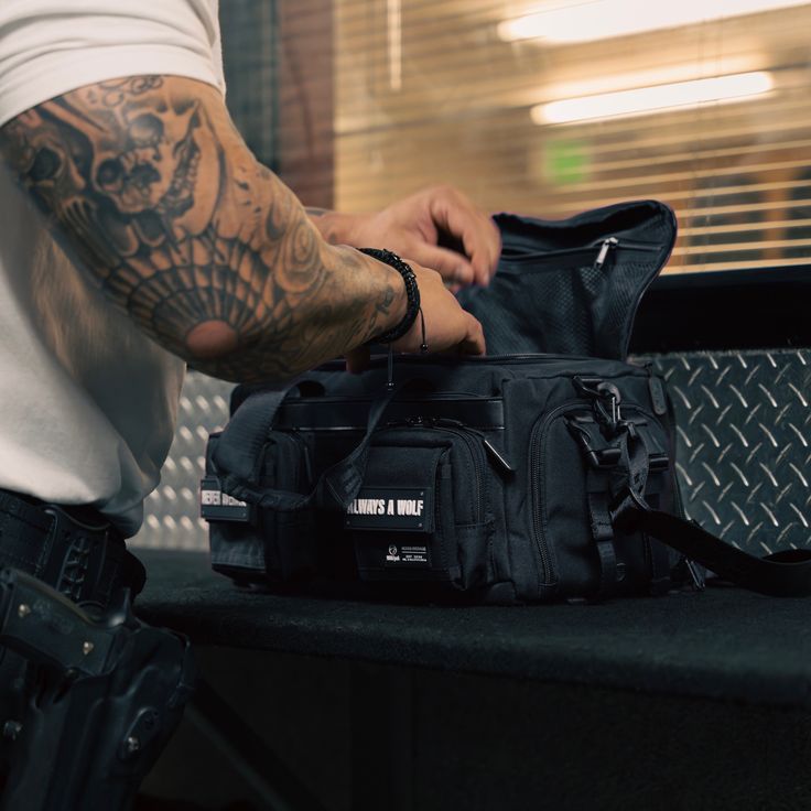 a man with tattoos on his arm holding a black bag