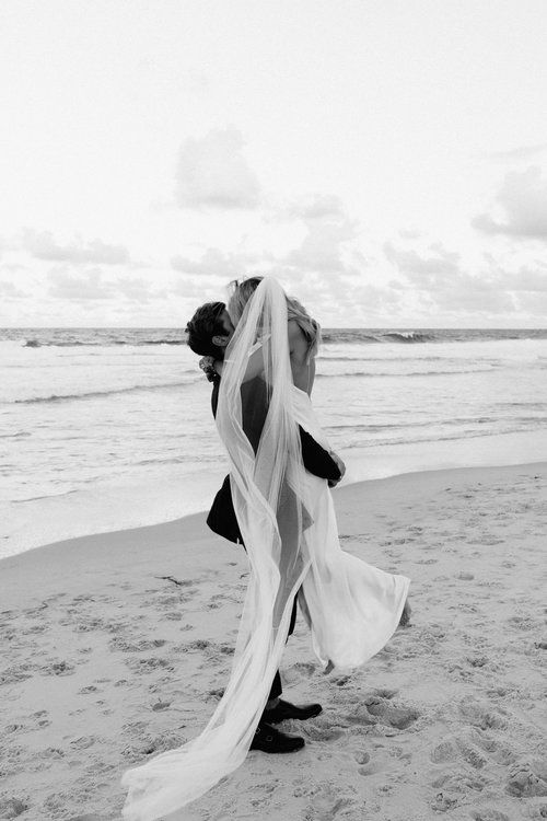 a bride and groom kissing on the beach