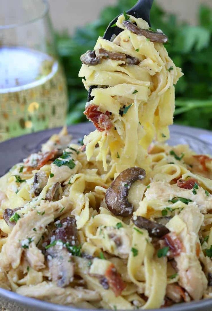 a fork full of pasta with mushrooms and parmesan cheese on it is being lifted from the plate