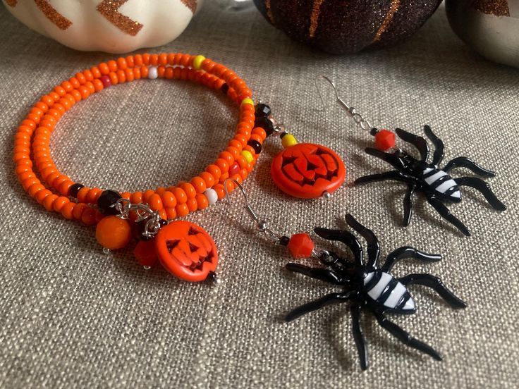 Perfect orange and assorted charms make this pumpkin/jack-o-lantern bracelet so adorable! The two bracelets are made from orange seed beads, crystals and charms. The braided and twisted bracelet (made from memory wire) has orange and a dash of yellow and black seed beads with crystals that dangle at the end of each cuff. The jack-o-lanterns that hang from the other bracelet have crystals and charms added and it's made from stretchable silver- plated memory wire. Both bracelets come with black and white enameled spider charm earrings that have an added orange crystal to match the bracelets. These such fun and easy to wear! Handmade Orange Bracelets For Halloween, Halloween Orange Round Bead Jewelry, Halloween Orange Round Beads Jewelry, Orange Round Beads Jewelry For Halloween, Orange Beaded Bracelet With Lobster Clasp As Gift, Adjustable Orange Beaded Bracelet With Lobster Clasp, Twisted Bracelet, Pumpkin Jack, Orange Crystals