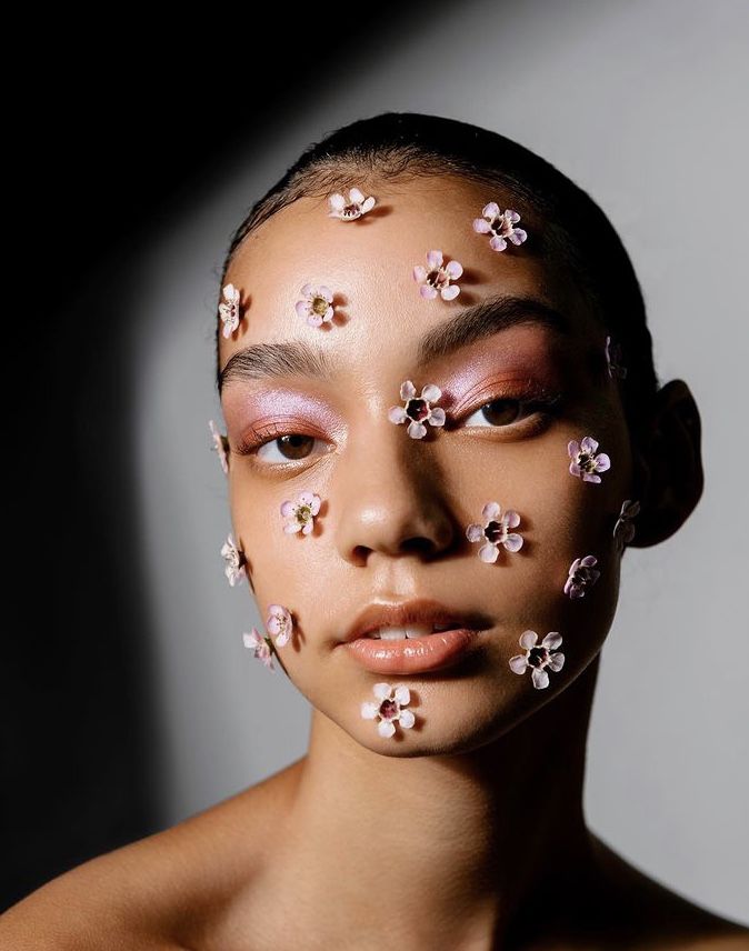 a woman with pink makeup and flowers on her face is shown from the front view