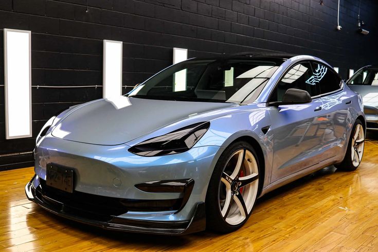 two electric cars parked in a garage with hard wood flooring and black brick walls