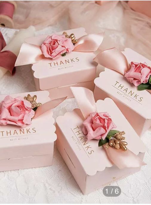 four pink boxes with flowers on them sitting on a white lace tablecloth next to teddy bears