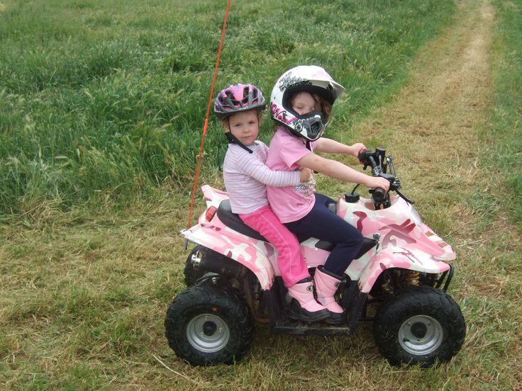 two children riding on four wheelers in the grass